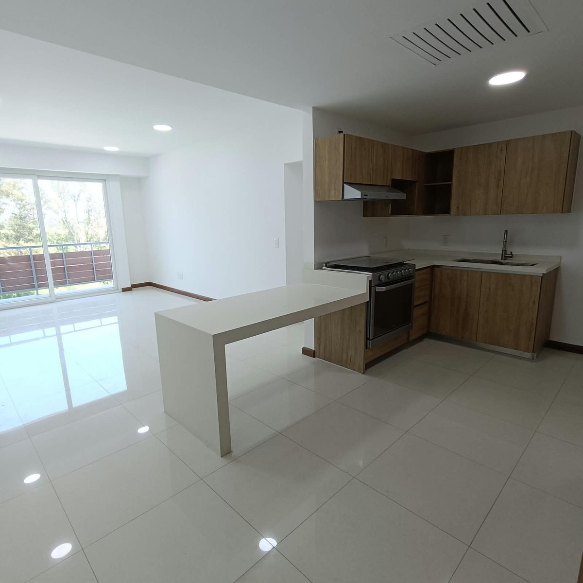 Sala y cocina integral con barra, y ventanal hacia el balcón