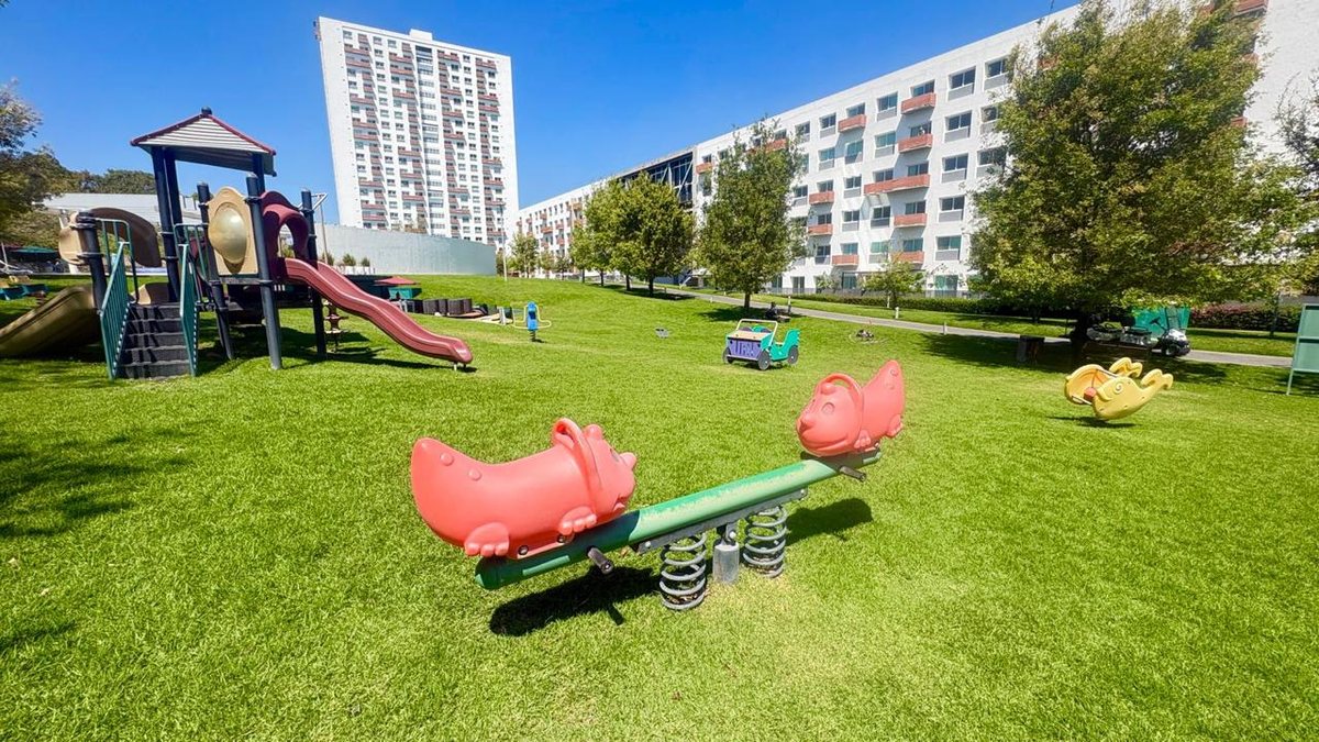 Área infantil con juegos sobre el pasto y las torres al fondo