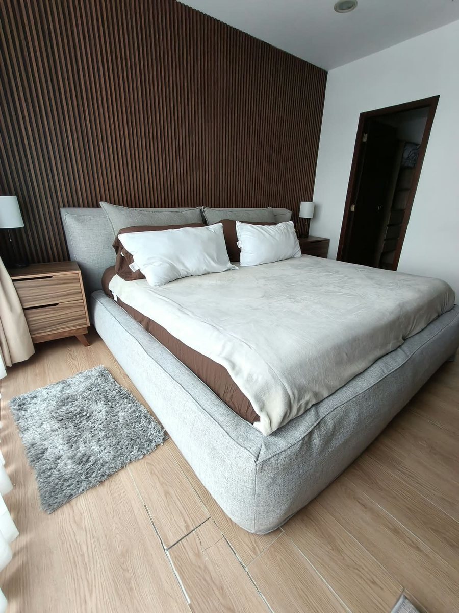 Recámara con cama matrimonial, burós y muro de madera