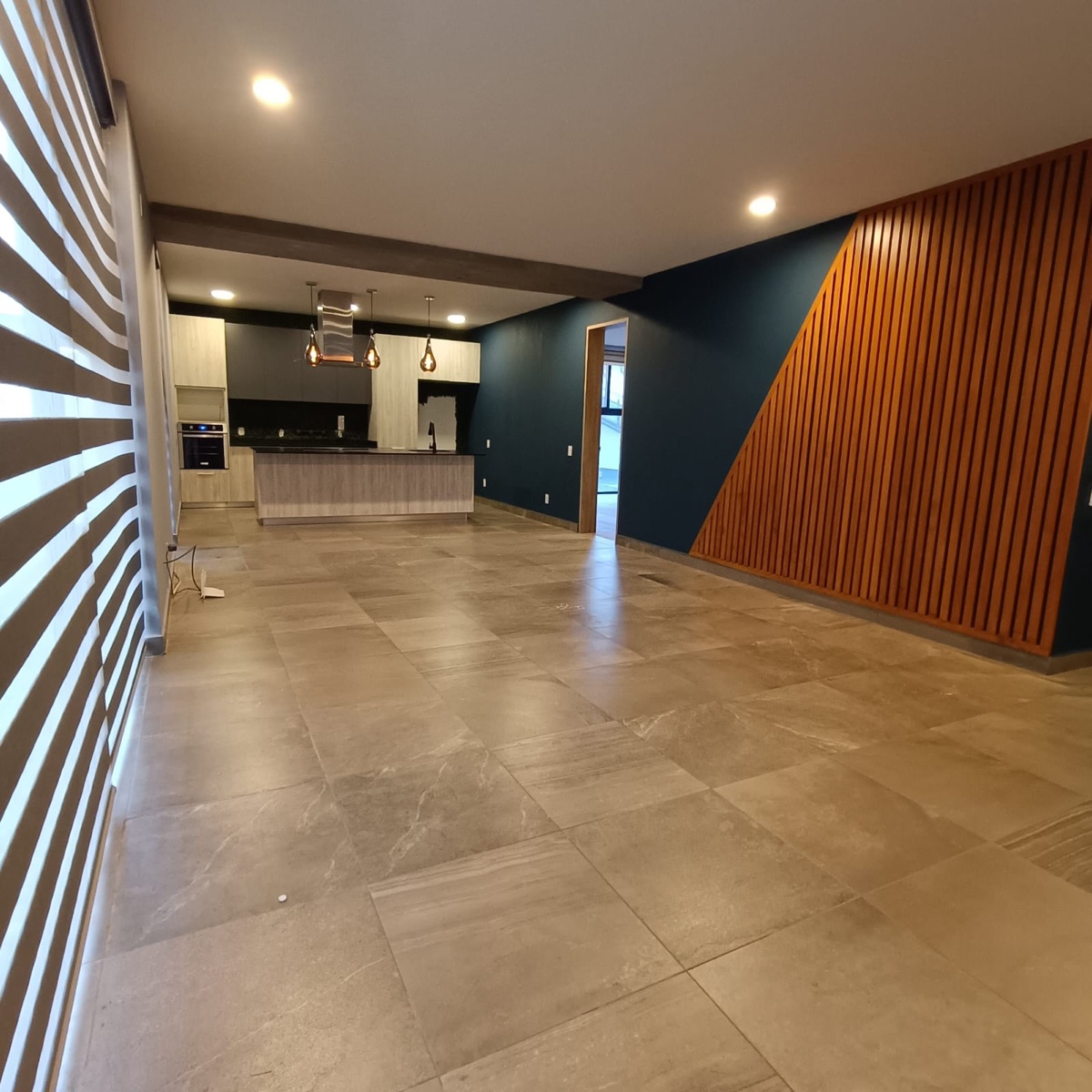 Sala y comedor amplios con piso de loseta, cocina al fondo y muro de madera