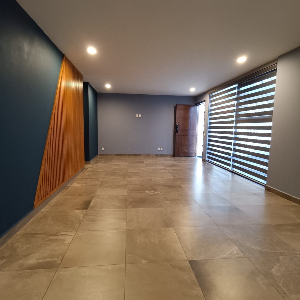 Sala hacia la puerta de entrada con persiana de doble tela y muro de madera