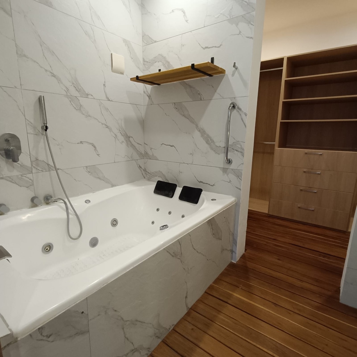 Baño principal con jacuzzi, muros de mármol y piso de madera
