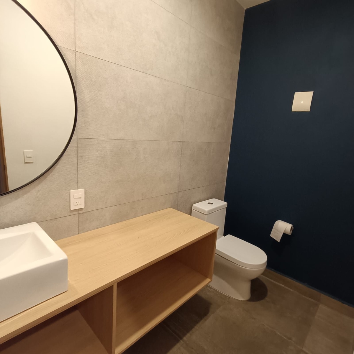 Medio baño de visita con lavabo, espejo redondo y mueble de madera