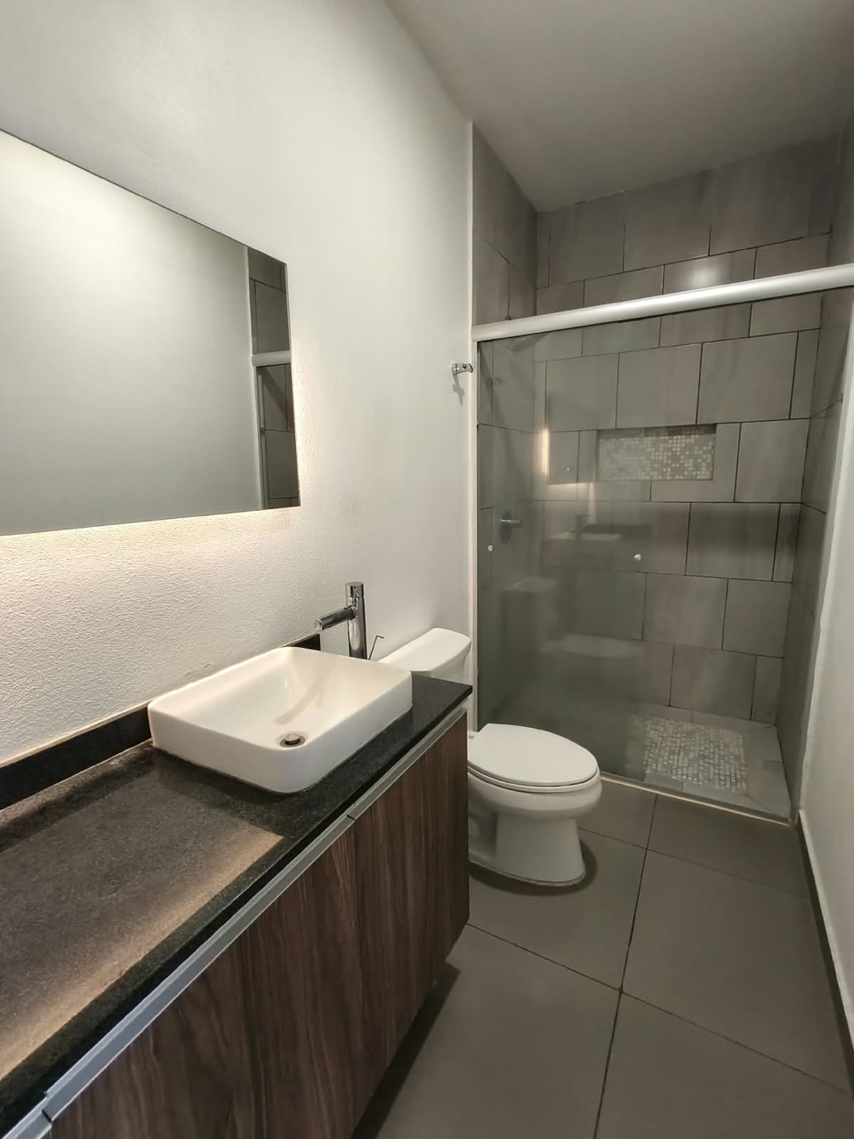 Baño con regadera de cristal, lavabo y espejo con luz