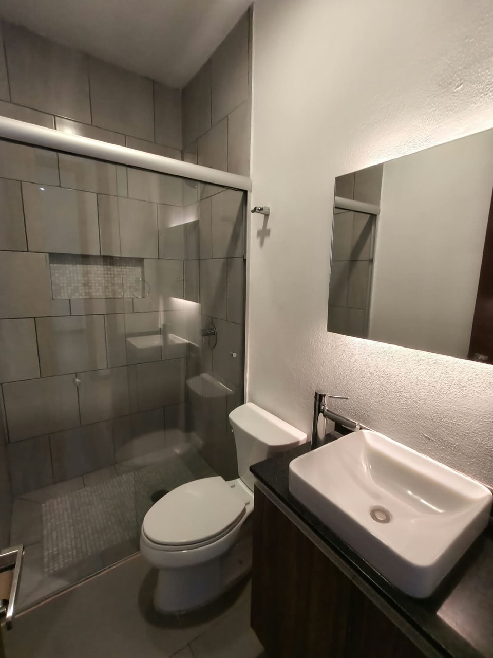 Baño con lavabo de cerámica, mueble de madera y regadera