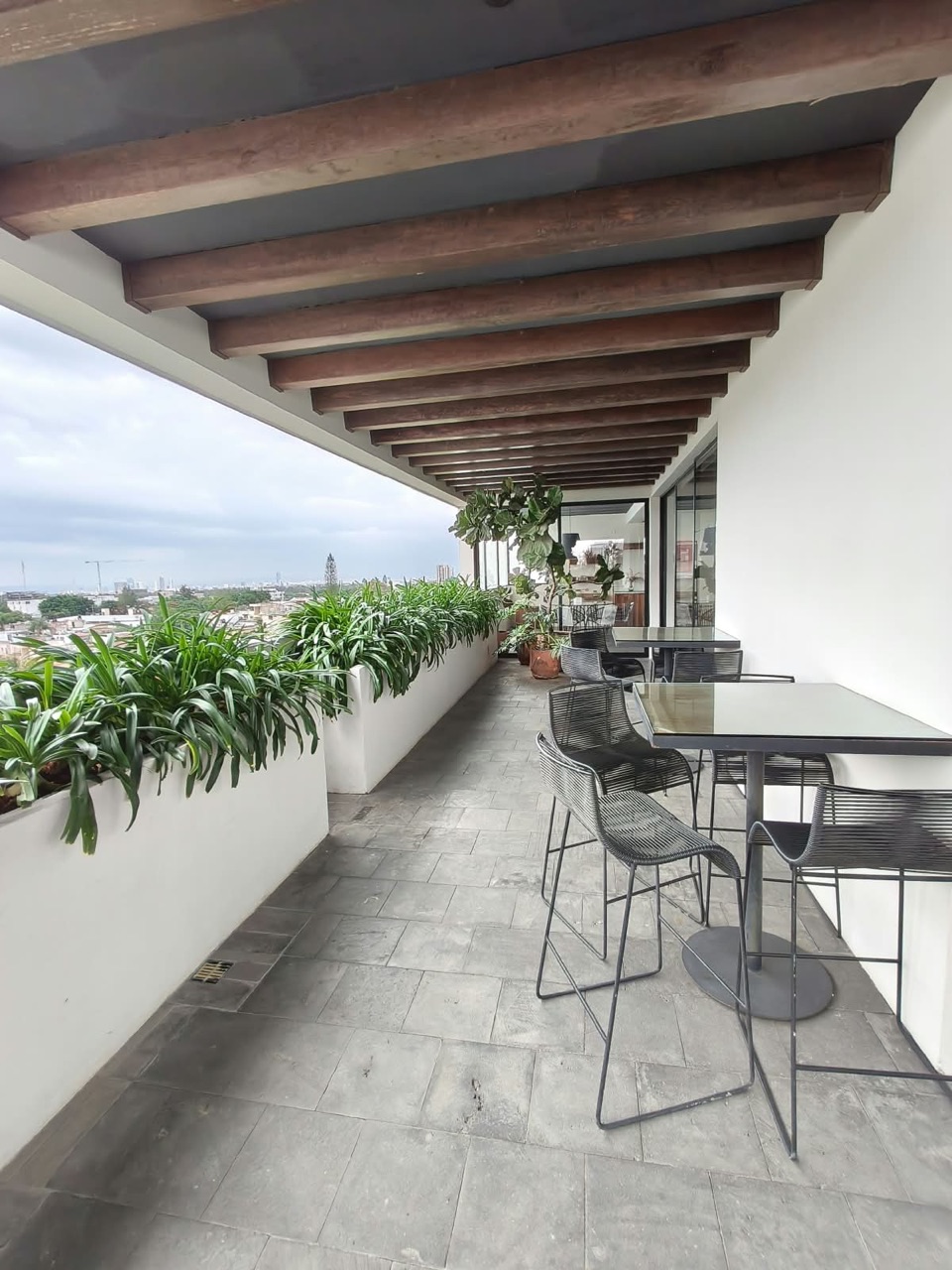 Terraza común con mesas altas, jardineras y vista a la ciudad