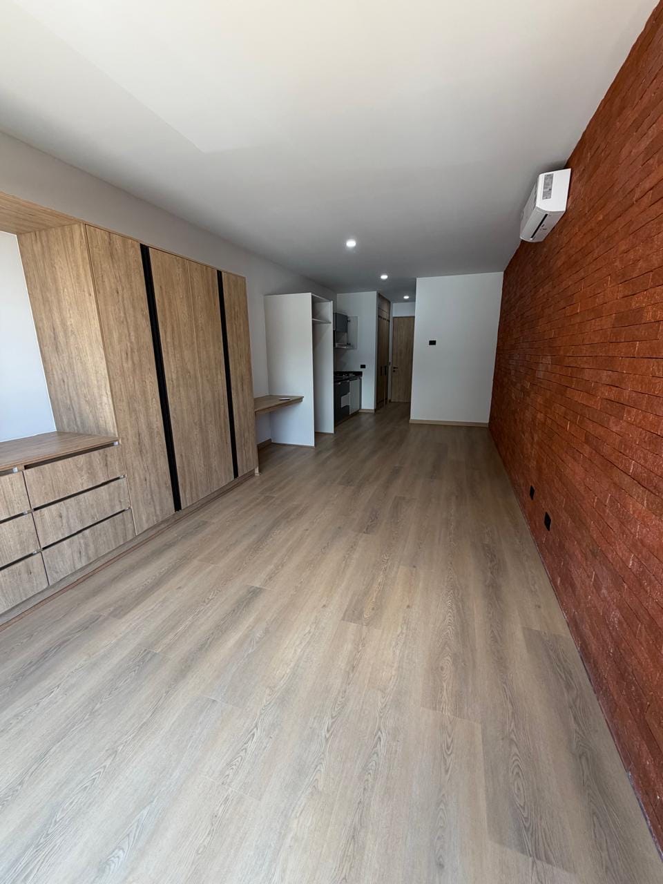 Estudio con muro de ladrillo, clóset y cocina al fondo