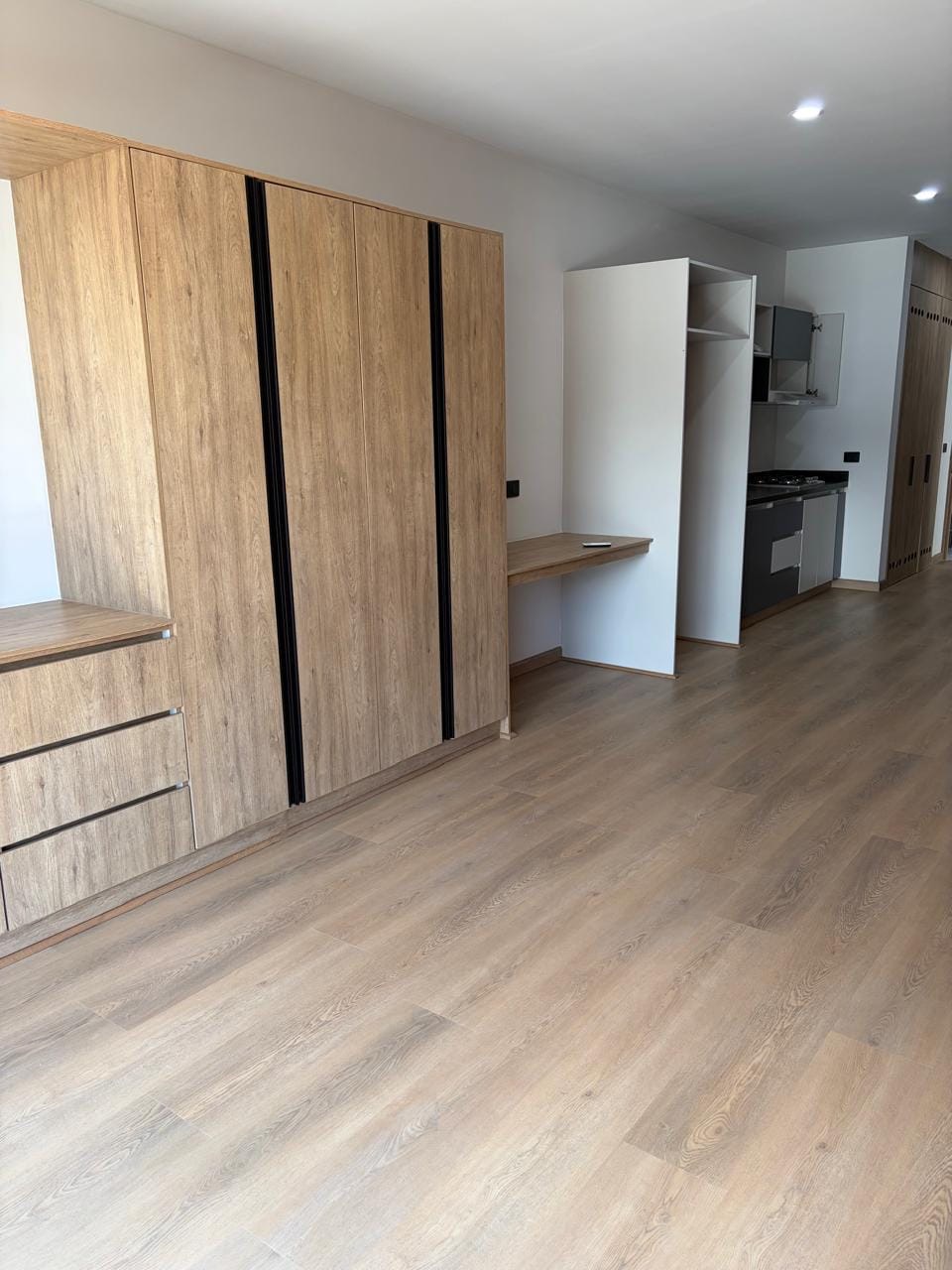 Clóset de madera con cajones, escritorio y cocina al fondo