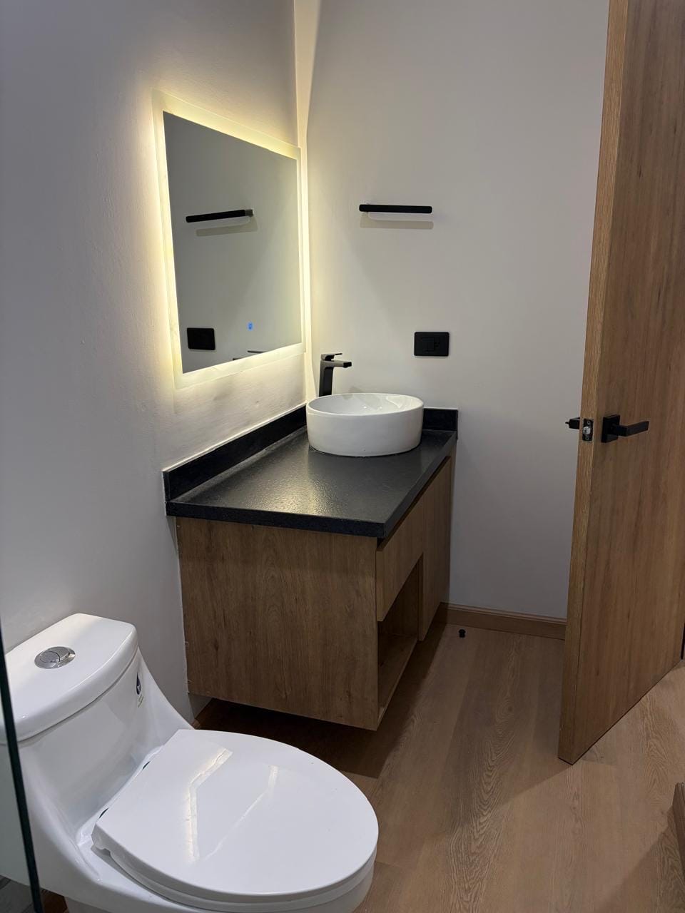 Baño con lavabo, espejo con luz y mueble de madera
